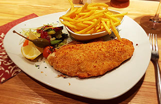 Bildbeschreibung: paniertes Schweinsschnitzel mit Pommes frites und verschiedenen Gemüsen.
