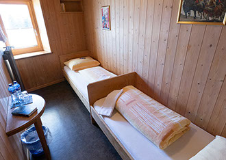 Bildbeschreibung: rustikales Hotelzimmer mit zwei Betten hinereinander im Berghotel Sartons, Valbella.
